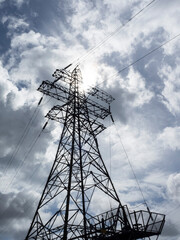 An electricity pylon viewed from its base looking upwards into a cloudy sky with the sun peeping through the clouds