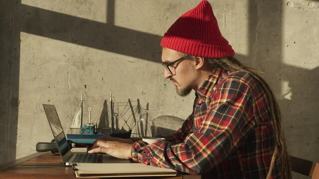Cheerful american hipster working remotely from home on netbook laptop, smiling male freelancer remote social distance work from home during coronavirus covid 19 pandemic