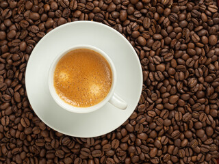 white cup with coffee, stands on coffee beans in soft focus, top view, copy space