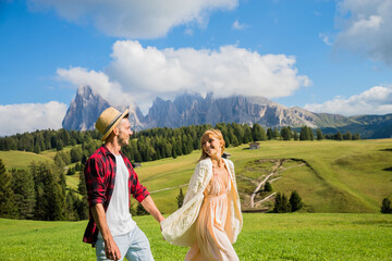 Fototapeta premium Romantic couple enjoying freedom walking on the hill. Boyfriend and girlfriend in love having fun hiking Siusi alps. Wanderlust and people concept.