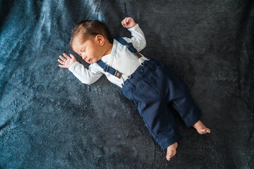 One month old baby lying on a gray velvet blanket sleeping. The baby is wearing a white t-shirt...