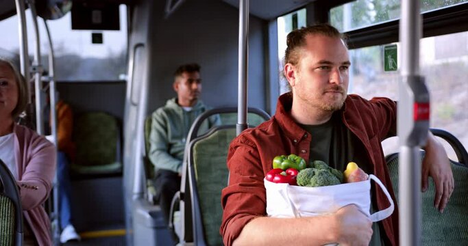 Man sitting inside public bus holding groceries shopping bag