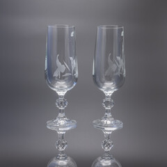 Two glass tall glasses for wine on a black background. The legs are faceted, the wine glasses are decorated with floral patterns. Reflection.