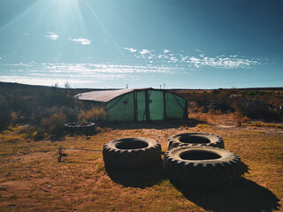 Vintage style image of farm with tractor tyres and a greenhouse. Blue sky and clouds, green grass,...