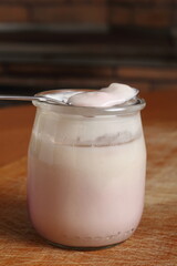 Spoon with yogurt on open small glass jar on wooden cutting boar