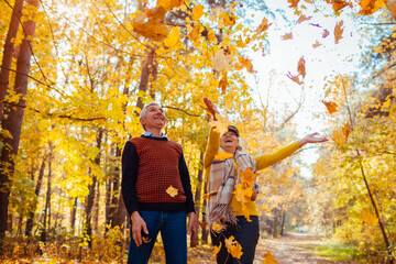 Fall season. Family couple throwing leaves in autumn forest. Senior people having fun outdoors...