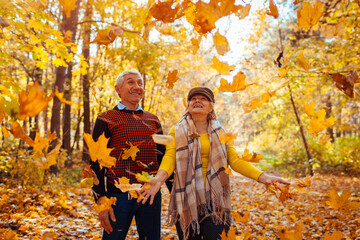 Fall season. Family couple throwing leaves in autumn forest. Senior people having fun outdoors...