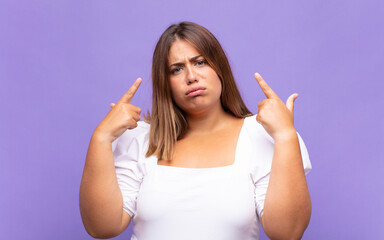 young blonde woman with a bad attitude looking proud and aggressive, pointing upwards or making fun...