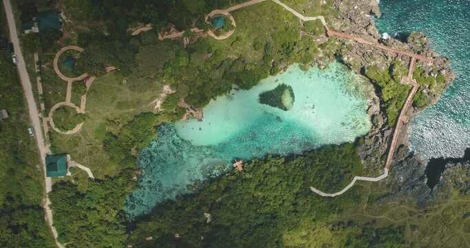 Top down of traditional Indonesian houses at limpid turquoise lake with designed ways on green valley in aerial view. Nobody Asia nature scenery of Weekuri lagoon, Sumba Island, Indonesia, Asia