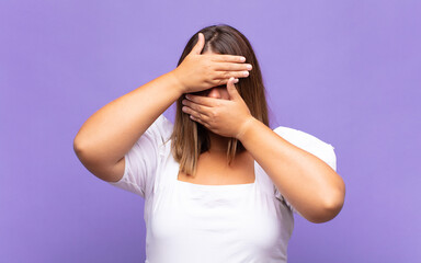 young blonde woman covering face with both hands saying no to the camera! refusing pictures or...