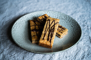 homemade proteein müsli bars with banana and oatmeal decorated with dark chocolate as a healthy alternative without sugar. lie on a rustic plate on a wrinkled linen tablecloth moody photography style