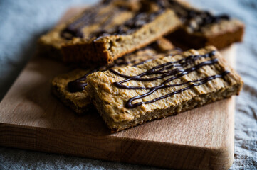 homemade proteein müsli bars with banana and oatmeal decorated with dark chocolate as a healthy alternative without sugar. lying on a rustic wooden board on a wrinkled linen tablecloth detail view