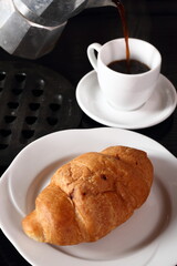 Croissant and pouring coffee from moka pot into cup