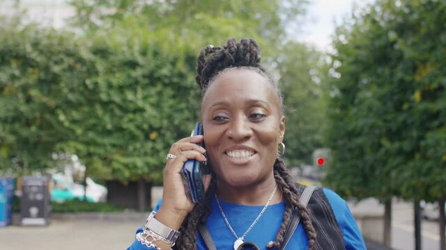Mature older black female talks on her phone as she walks through town