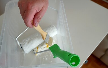 A man picking a paintbrush from a container with painting equipment such as paint rollers. He is...