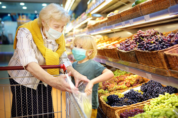 Senior woman and her grandchild wearing disposable medical mask shopping in grocery supermarket...