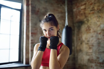 Obraz premium Young woman ready for hits punching bag during a boxing training. Female boxer doing fitness.