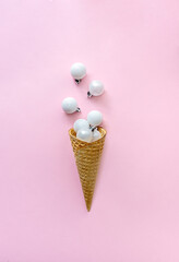 White glitter Christmas decoration baubles in ice cream cone on pink background. Creative concept for new year.