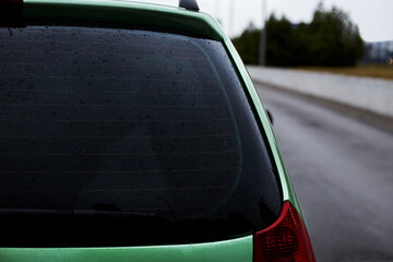 Back window of green car parked on the street in autumn rainy day, rear view. Mock-up for sticker or decals