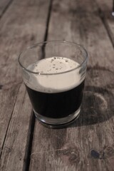 glass with dark beer anf foam on woodeb table sepia colours