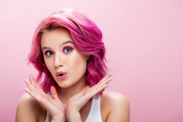 Naklejka premium surprised young woman with colorful hair and makeup posing with hands near face isolated on pink