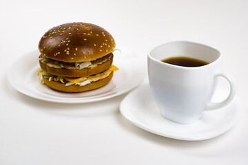 Burger and a cup of coffee. Burger on a white plate and coffee in a white cup.