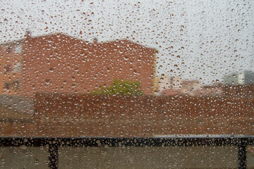 glass window with raindrops from which you can see a railing and a brick building