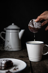 Homemade chocolate cookie soaked in milk in white and blue cup on old wooden table on dark background .