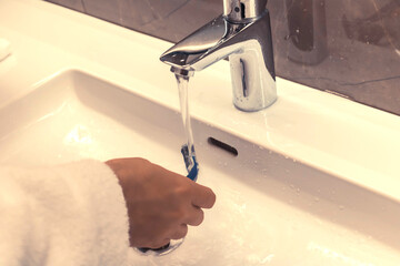 Close-up of man rinsing razor in bathroom sink while shaving in the morning.