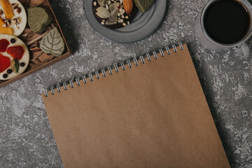 Chocolates with dried fruits in a box and craft paper notebook near the cup of coffee. Place for your text.