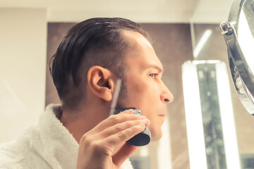 Close-up of man using electric razor while shaving in the bathroom.