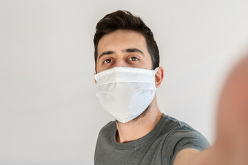 Man wearing face mask taking a selfie. White background.
