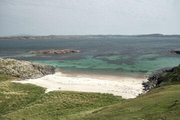 A sunny and isolated empty beach on the coast of the Isle of Iona, Scotland. Cinematic film colour grading and a rugged shoreline make for a relaxing and calming photo. View over the Atlantic Ocean.