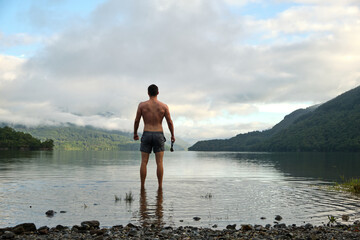 A muscular mid 20s male stands confidently after wild swimming in Loch Lomond, Scotland. Wearing...