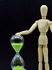 maniquí de madera y un reloj de arena con fondo negro