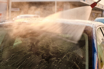Car washing under high pressure water at sunset. Manual car cleaning system outdoor. Self service car washing concept. 