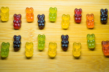 Many gummy bears of different colors and flavors on a wooden background.