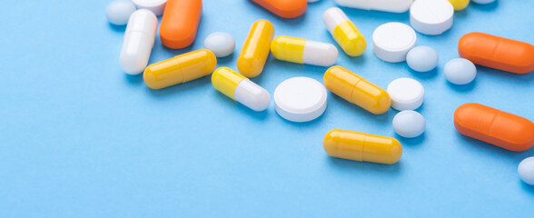 Multicolor tablets and pills capsules on blue background Heap of assorted various medicine tablets and pills. Horizontal banner