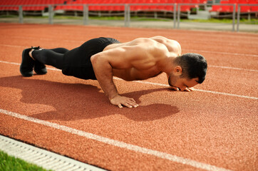 Young athletic man doing push-up exercise in the stadium. Training with your own body weight. Healthy lifestyle. Outdoor sports activities. 