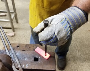 Blacksmith drifting a hole in steel at the anvil in apron and clove.