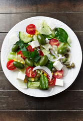 Healthy Salad with Feta Cheese, Green Olives, Baby Spinach, Cucumber, Cherry Tomatoes and Capers. Rustic wooden background. Top view. 