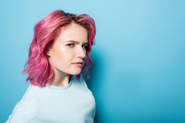 tense young woman with pink hair on blue background