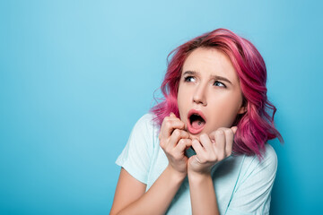 scared young woman with pink hair on blue background