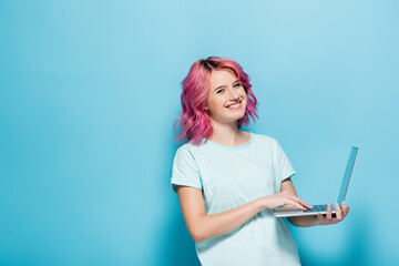 young woman with pink hair using laptop on blue background