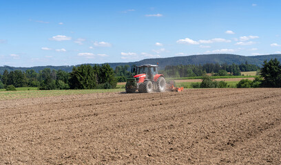 Traktor mit Egge arbeitet im Sommer auf einem Feld aus brauner Erde