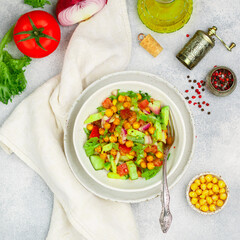 Healthy delicious vegetarian or vegan salad with chickpeas, lettuce, avocado, cucumber, tomatoes, red onion, olive oil and spices. Selective focus, copy space, top view