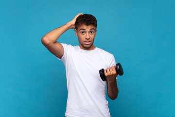 young man lifting a sumbbell feeling stressed, worried, anxious or scared, with hands on head,...