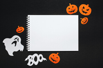 Happy halloween holiday concept. Notepad with text on black background with bats, pumpkins and ghosts
