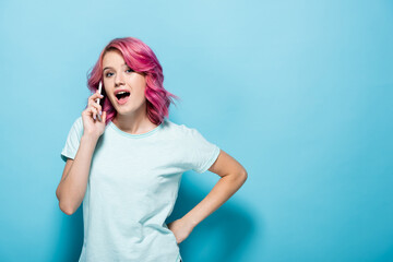 young woman with pink hair talking on smartphone with open mouth on blue background