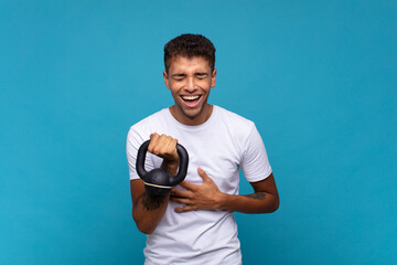 young man lifting a sumbbell laughing out loud at some hilarious joke, feeling happy and cheerful,...